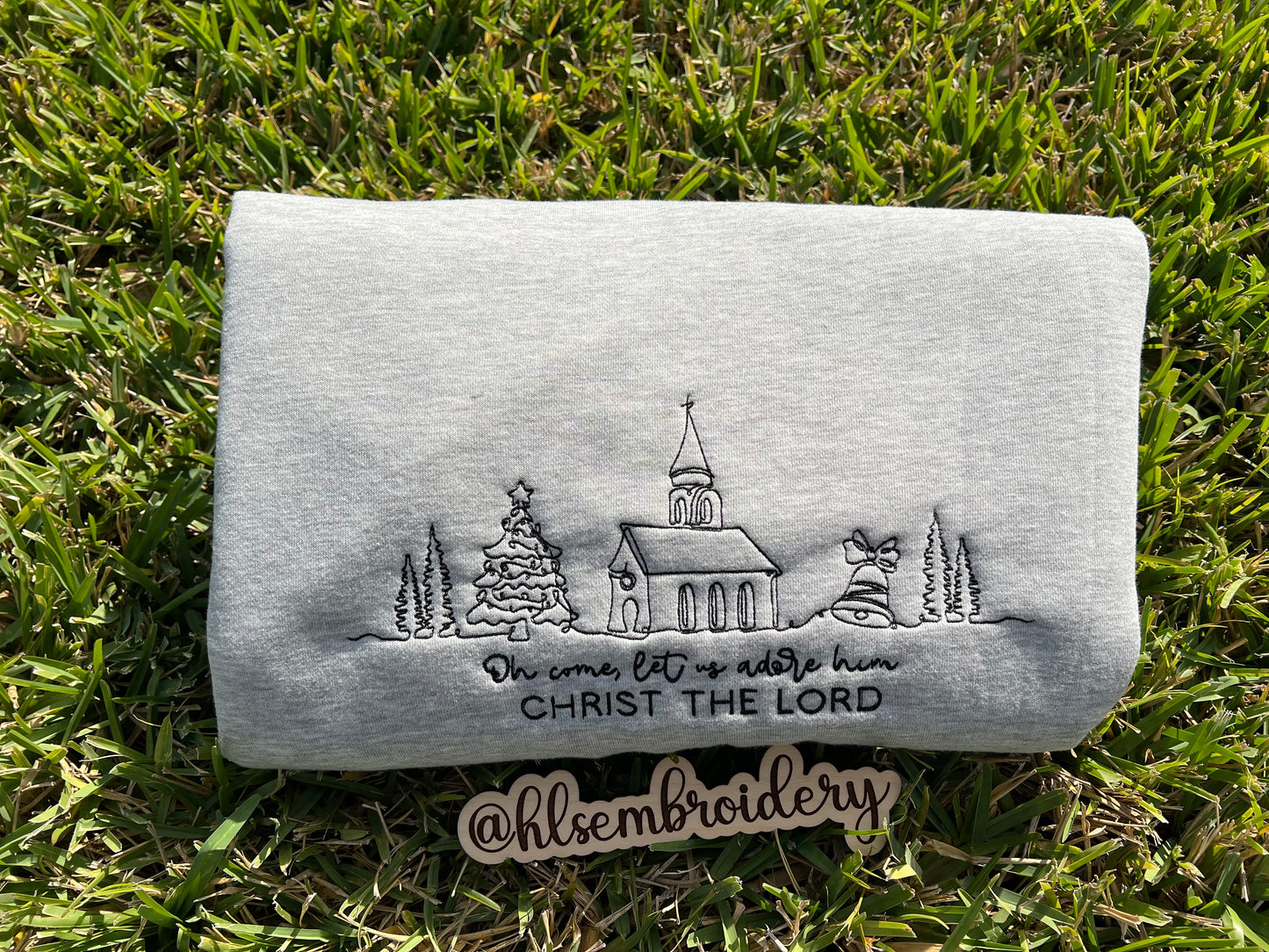 Embroidered Design That says Oh come, let us adore him Christ the lord on a gray fabric