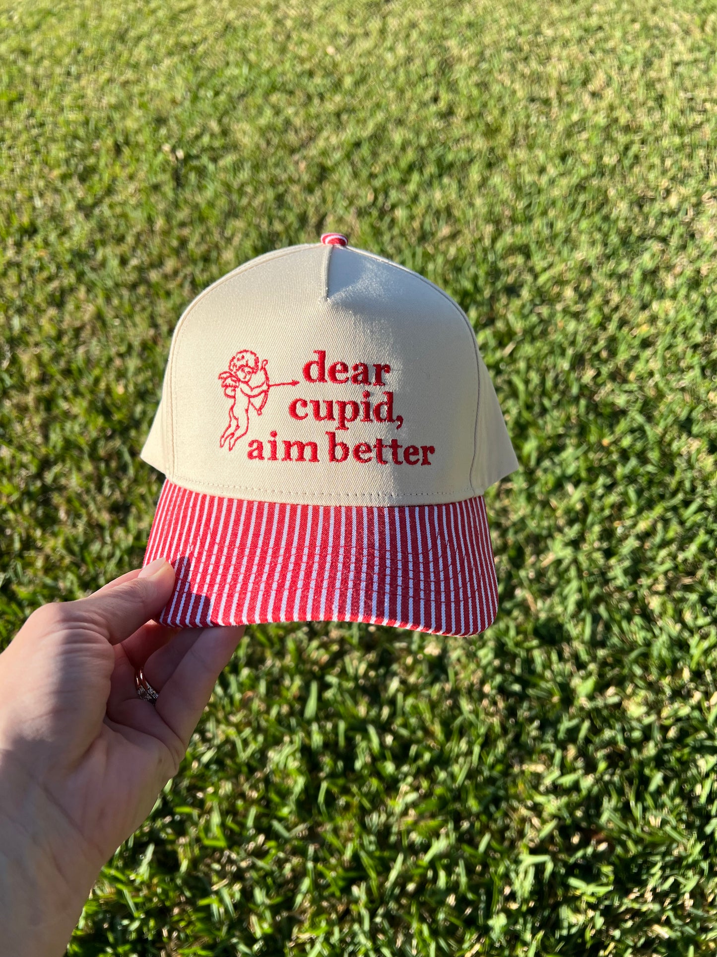 red and white stripe brim with beige Cap with 'dear cupid, aim better' text embroidered