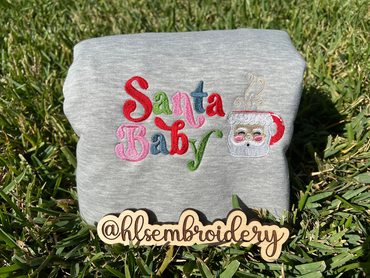 Gray fabric with 'Santa Baby' embroidery on grass.