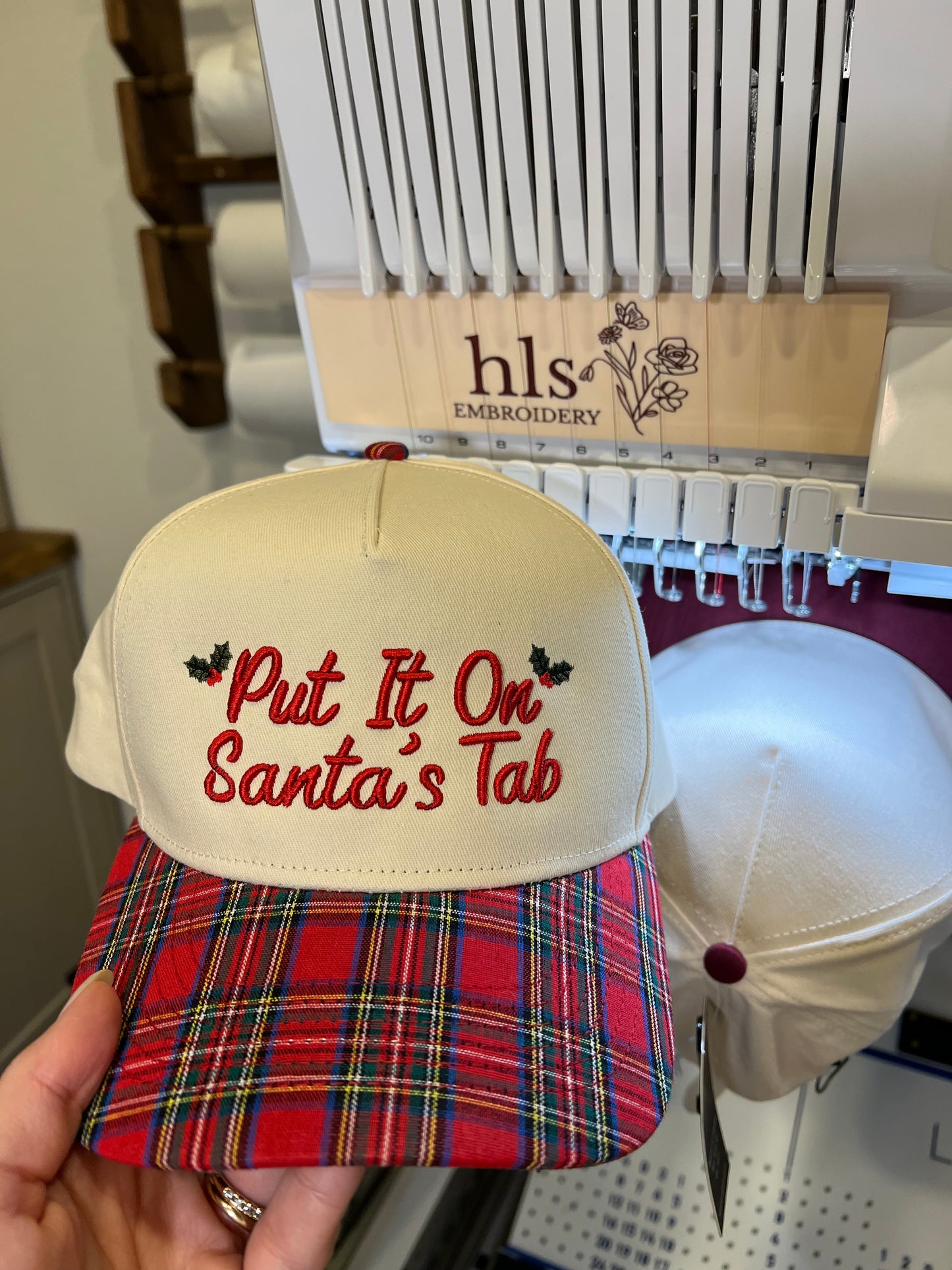 beige and plaid cap with the embroidery text on the front "put it on Santa's tab"