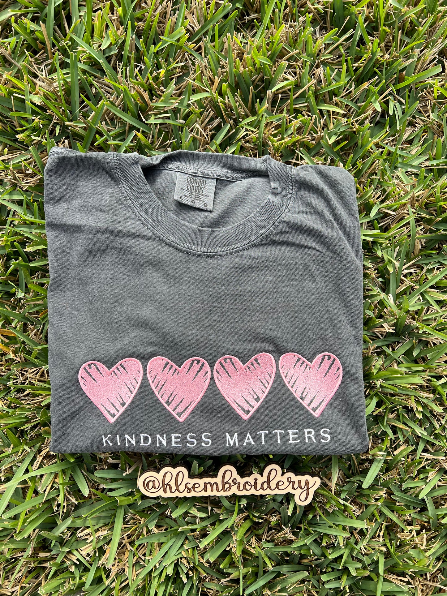 Folded color pepper comfort colors shirt with pink hearts and 'Kindness Matters' embroidered on it