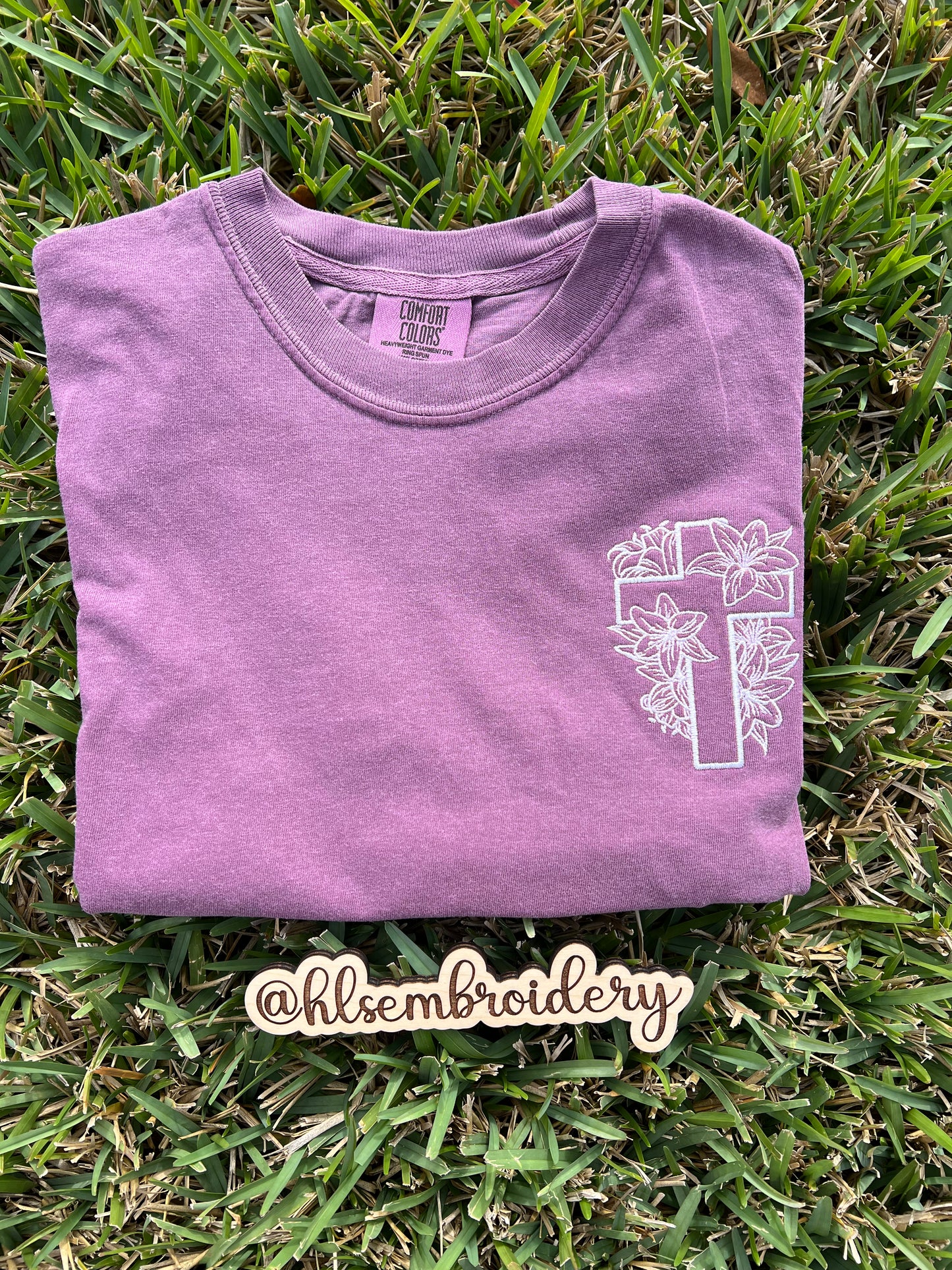 Comfort colors shirt berry with white floral cross design embroidered on it.