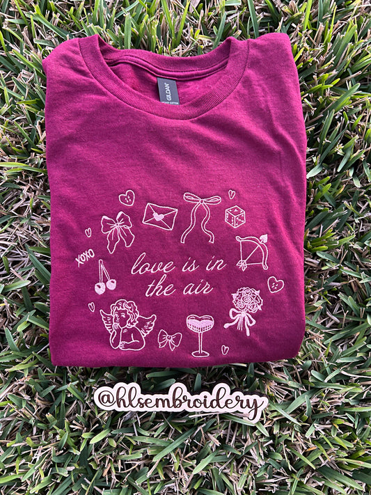 Maroon t-shirt with white embroidery Valentines Design with text Loe is in the air