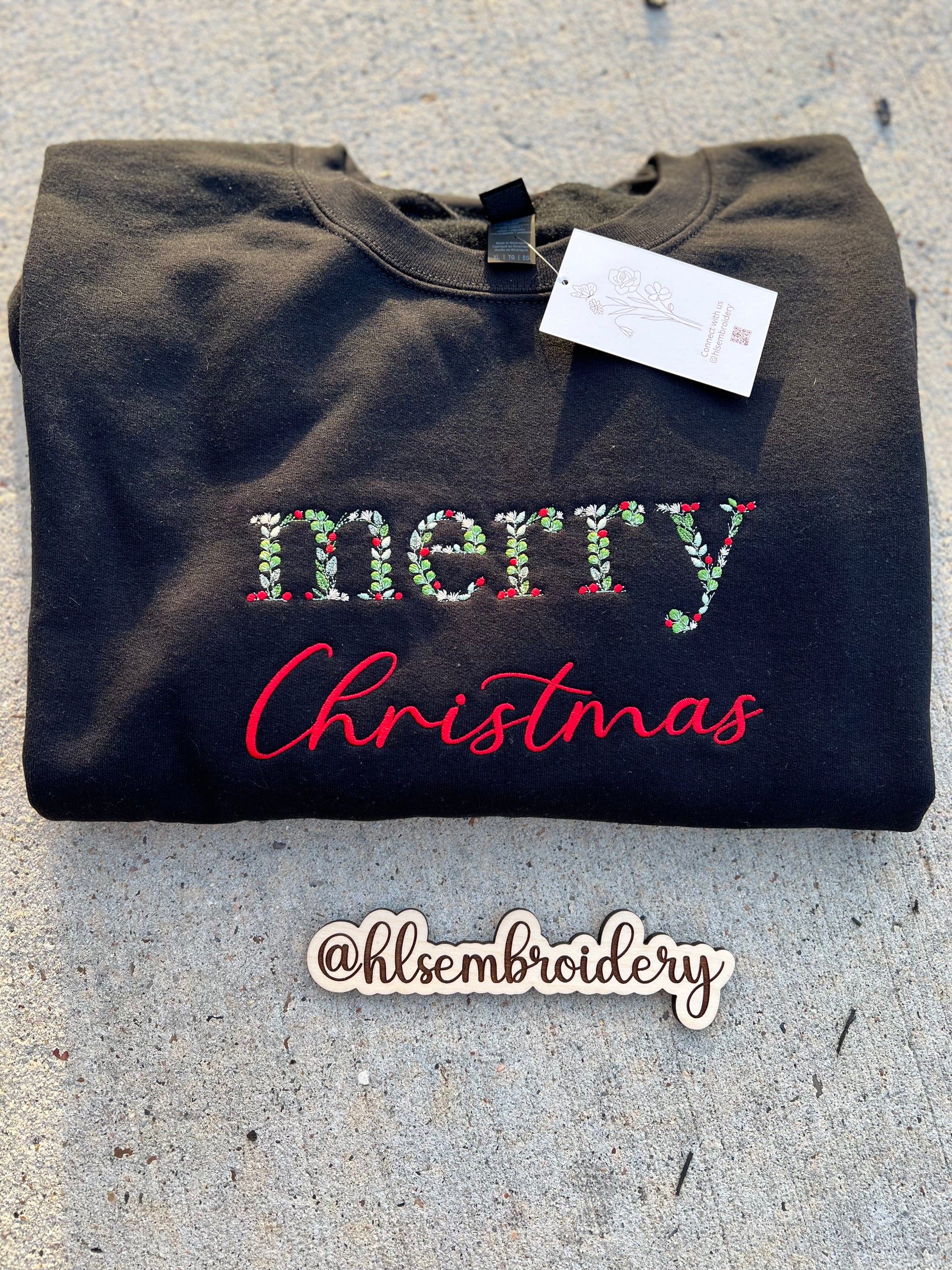 Black sweatshirt with 'Merry Christmas' embroidery on a concrete surface, 