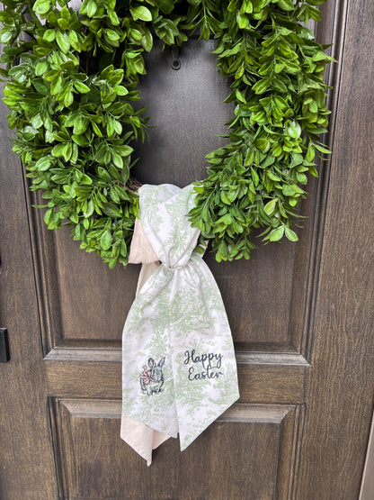 Green Toile Wreath sash with bunny and bow and happy Easter embroidered on it shown on a green wreath tied as an example of how to use it. 