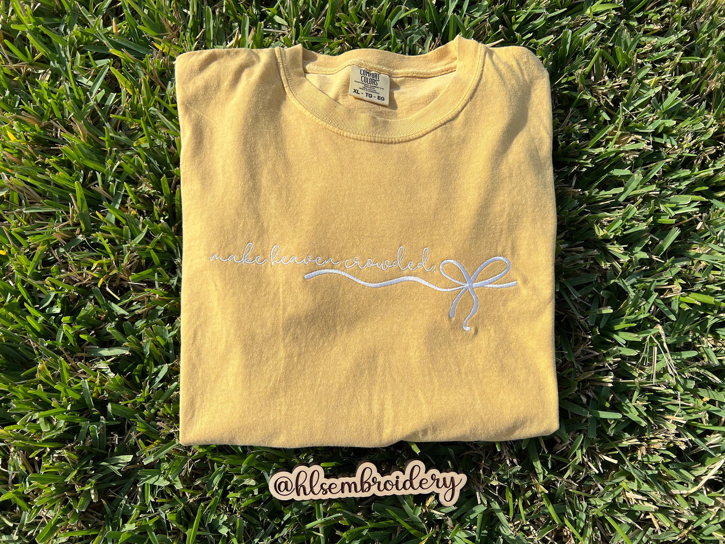 Folded yellow t-shirt with embroidery on grass, featuring a brand name.