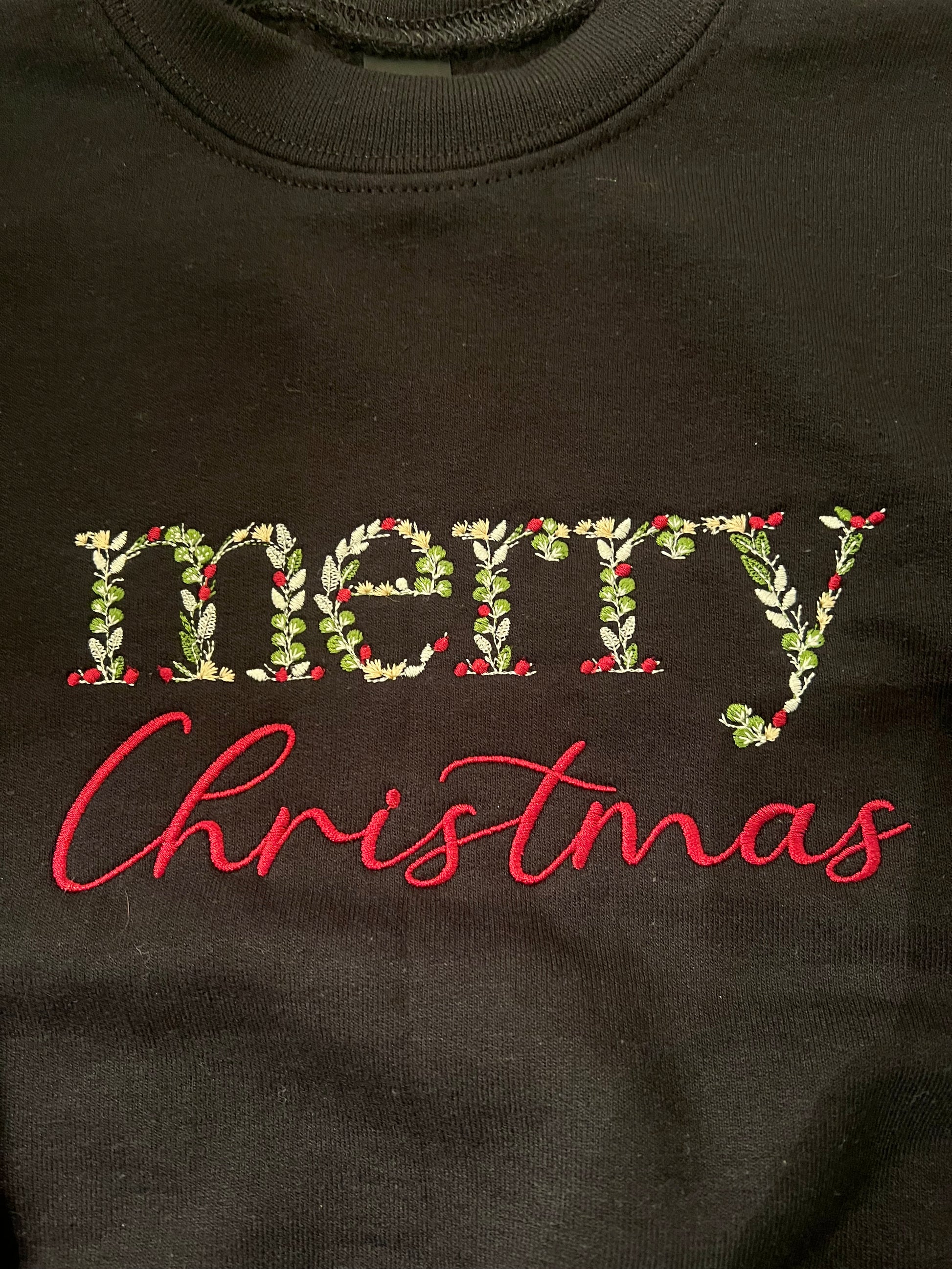 black sweatshirt with 'merry Christmas' text on a wooden surface