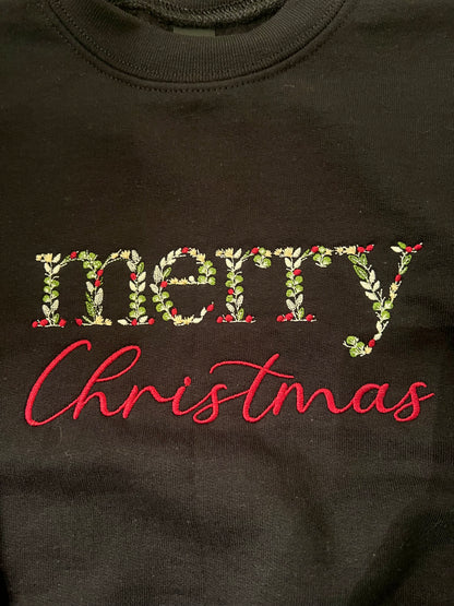 black sweatshirt with 'merry Christmas' text on a wooden surface