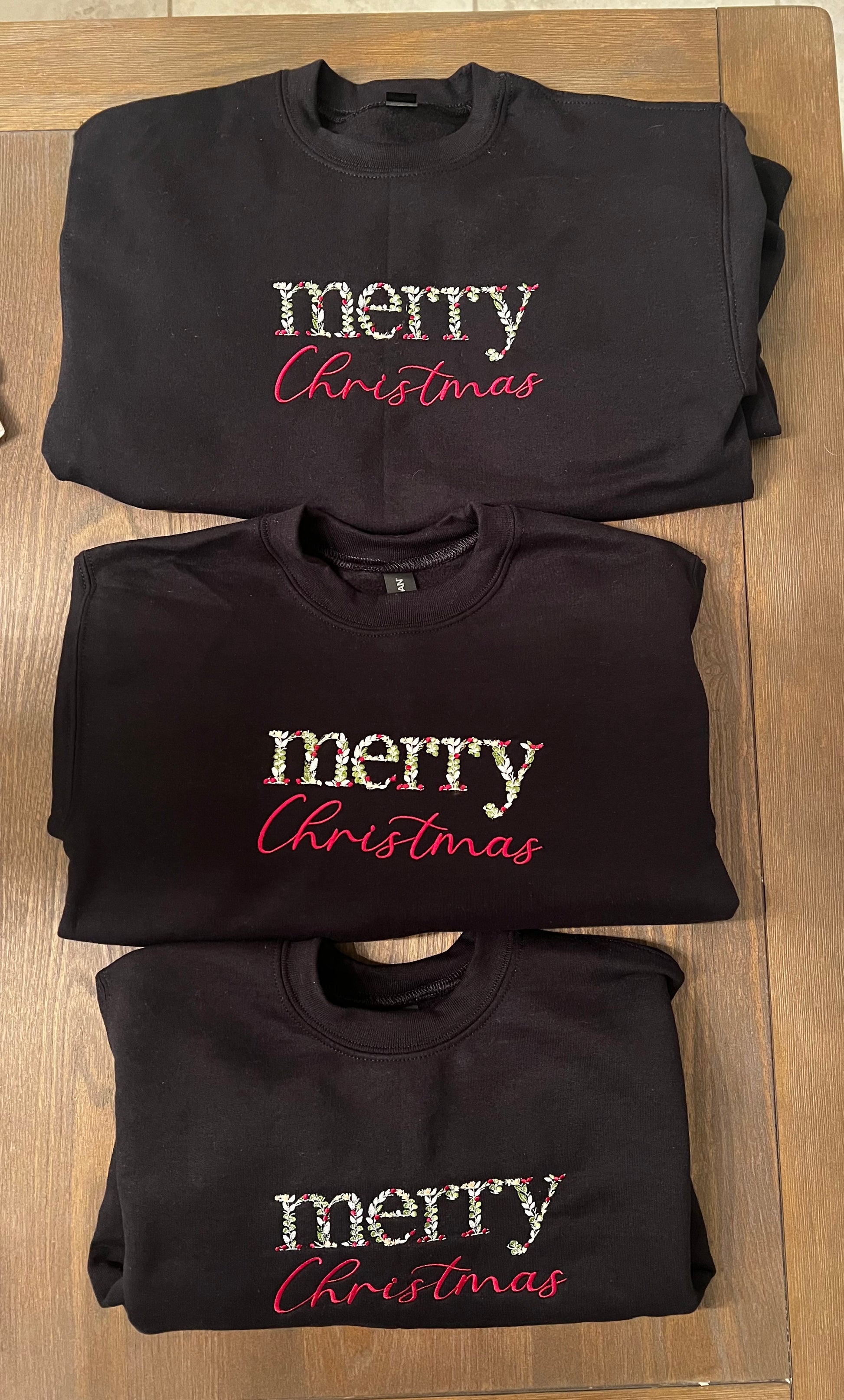 black sweatshirt with 'merry Christmas' text on a wooden surface