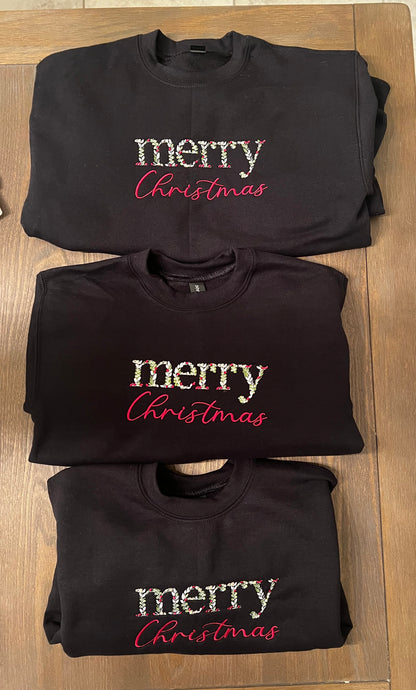 black sweatshirt with 'merry Christmas' text on a wooden surface