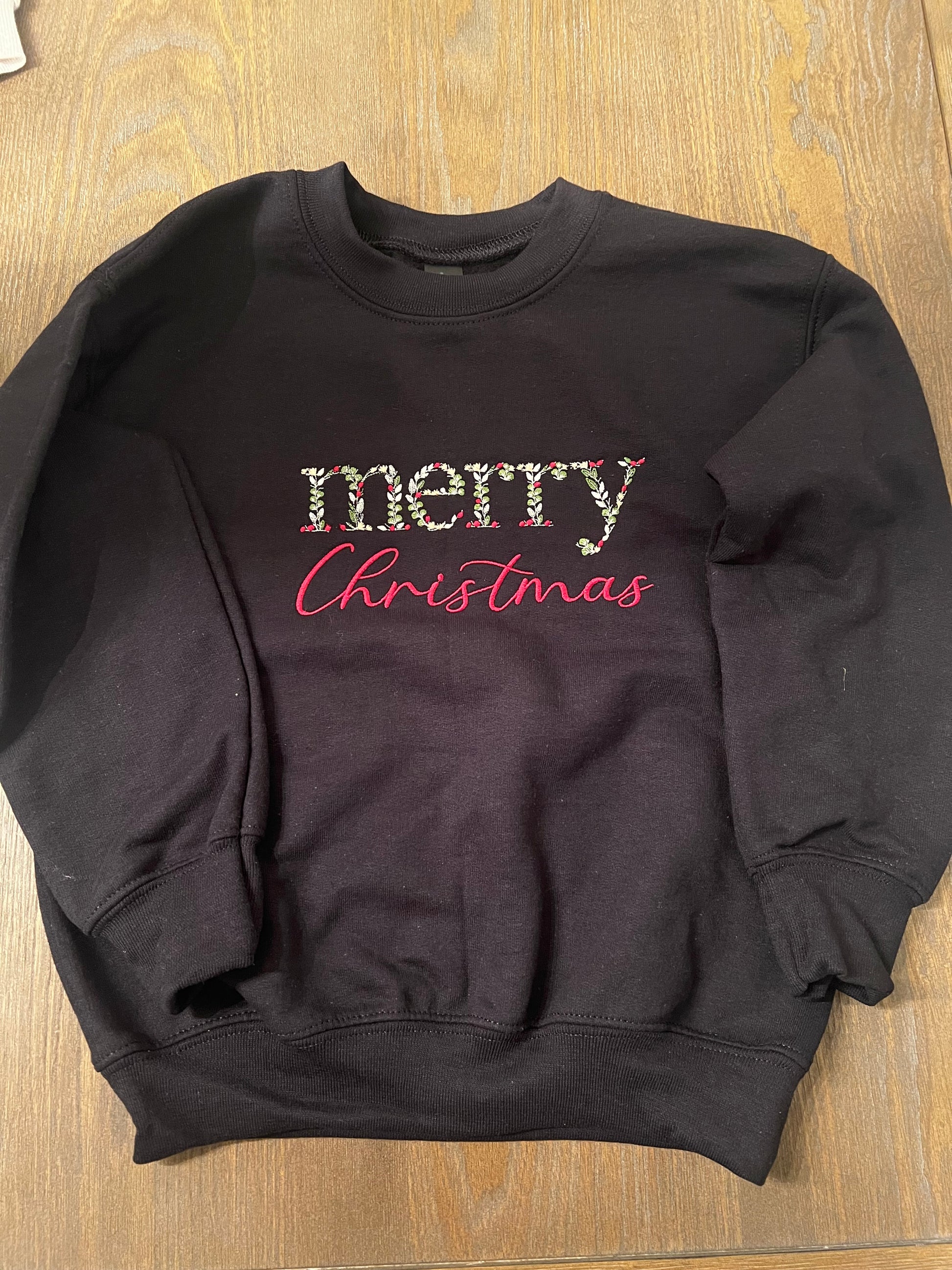Black shirt with 'Merry Christmas' text on a wooden surface