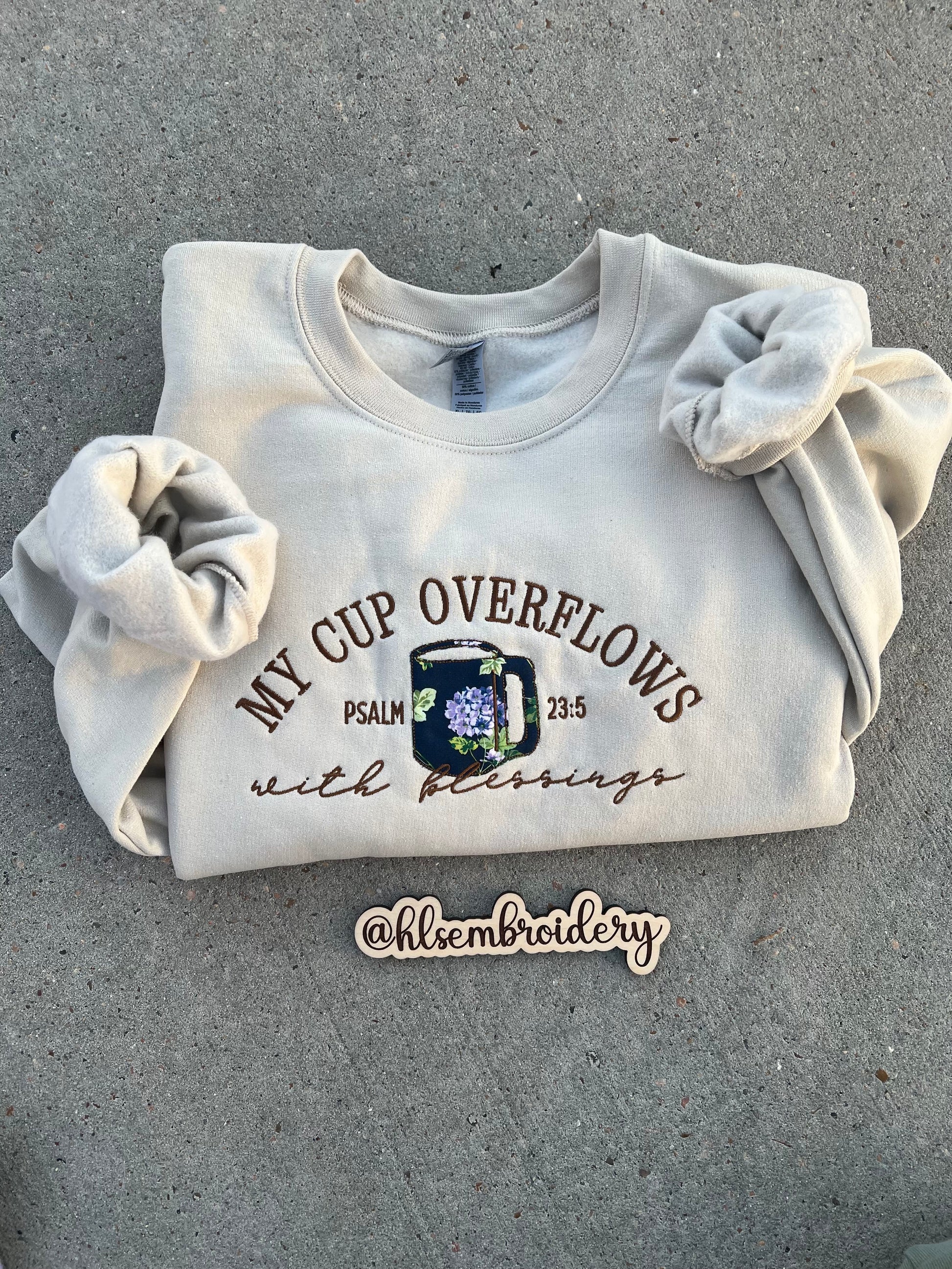 sand color crewneck embroidered using appliqué and regular embroider with text "My cup overflows with blessings" "Psalm 23:5)