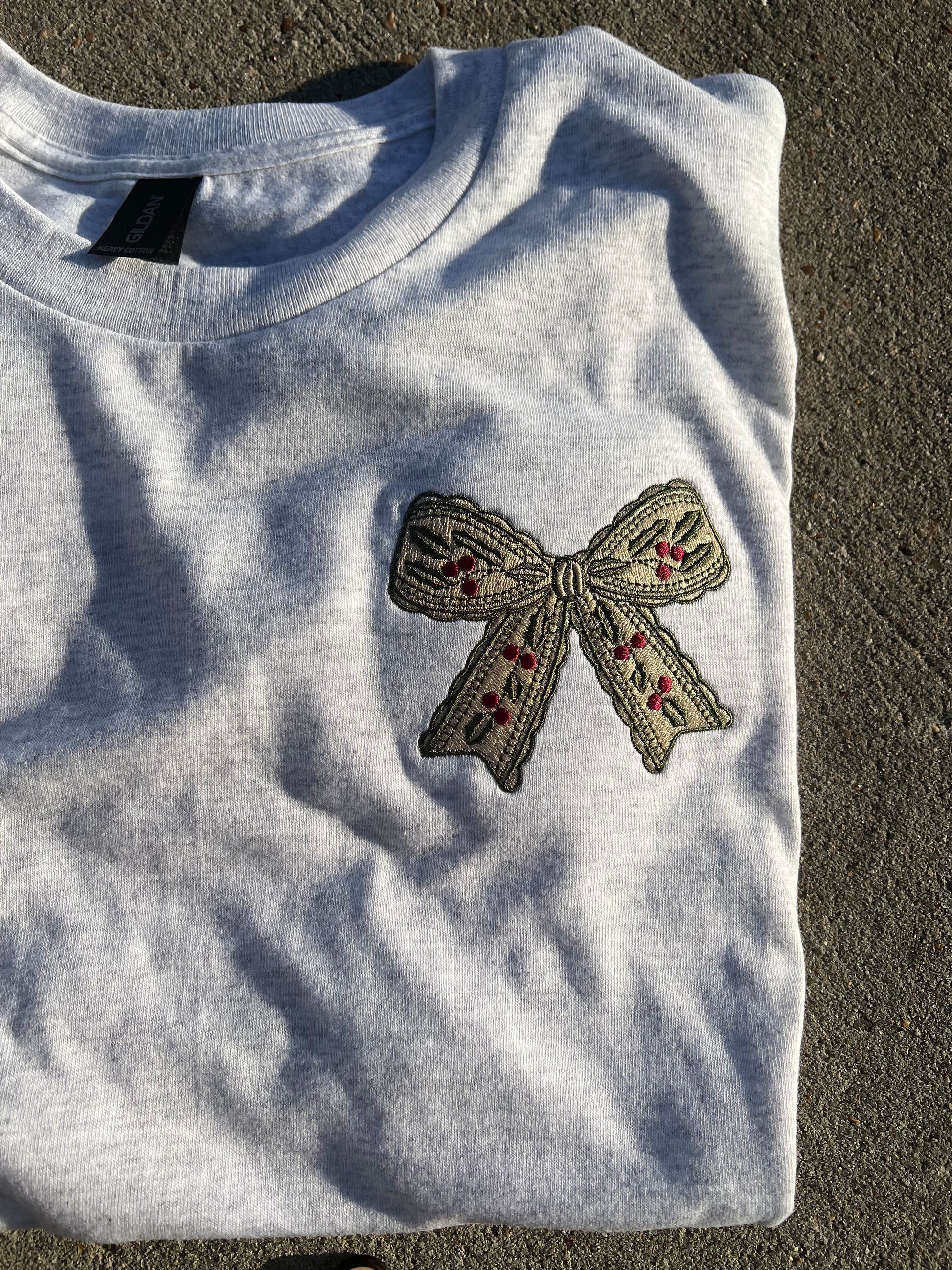 Embroidered bow design on a gray fabric with 'hlsembrodiery' branding.