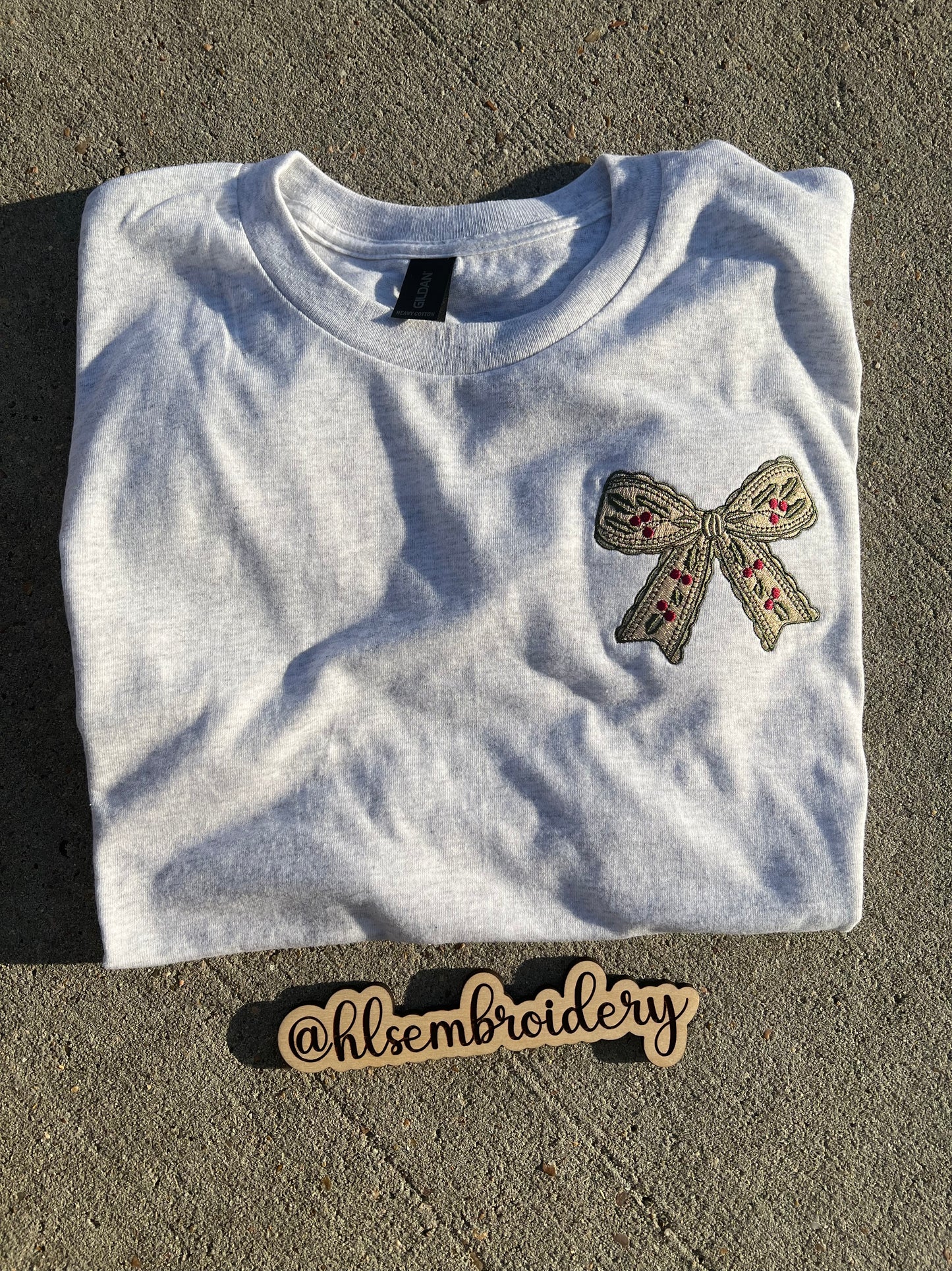 Embroidered bow design on a gray fabric with 'hlsembrodiery' branding.