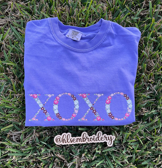 Folded purple shirt with floral 'XOXO' embroidered on the front