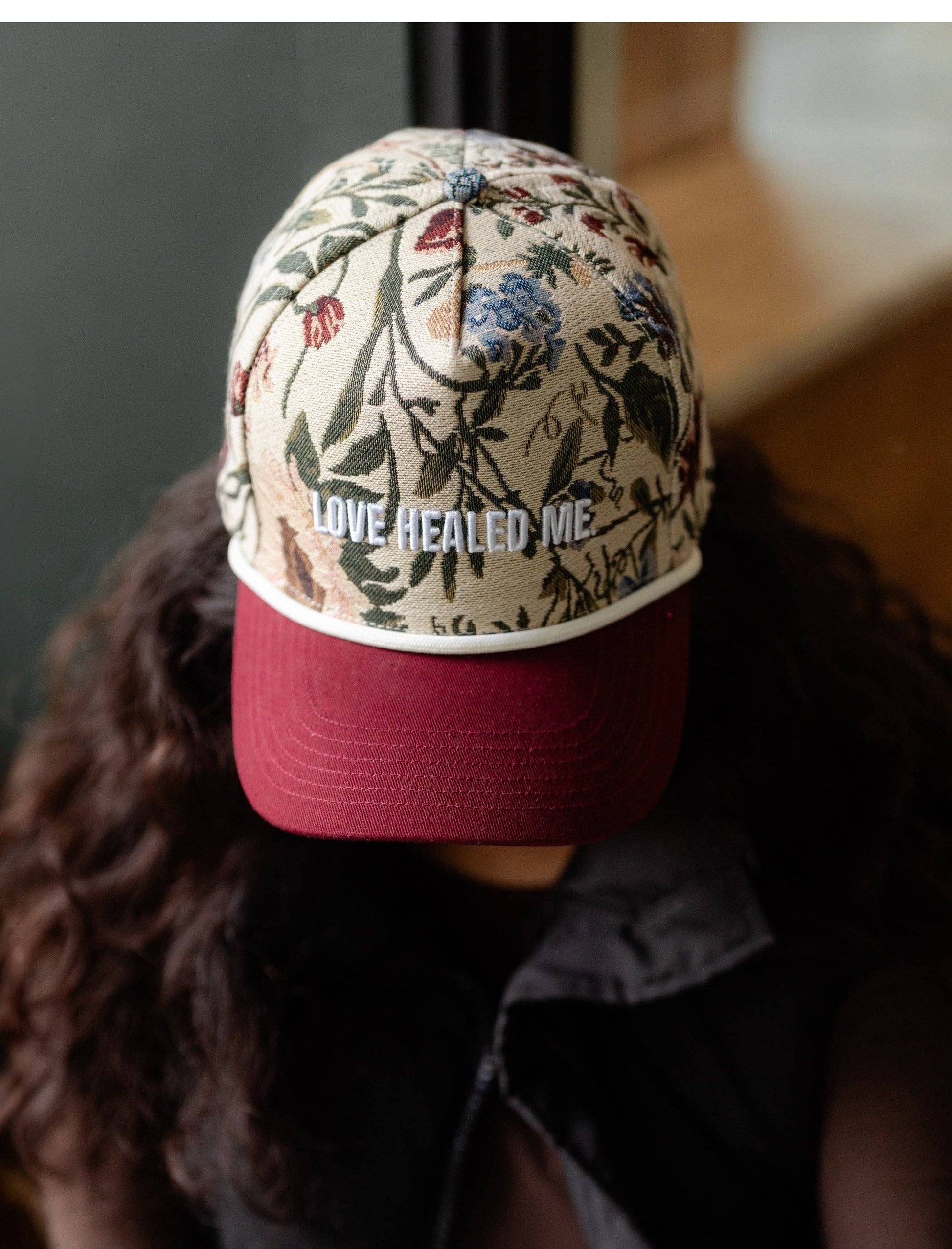 Person wearing a cap with floral patterns and 'Love healed me' text.