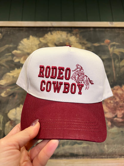 Cap with 'Rodeo Cowboy' text and logo held by a hand against a floral background