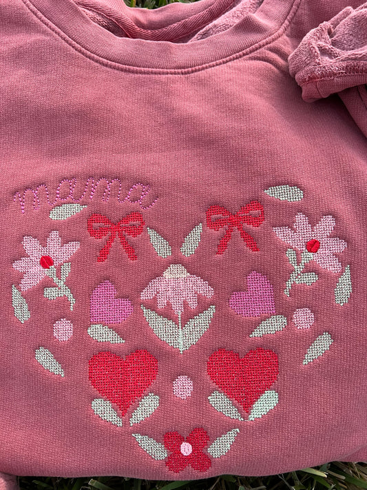 Close up of Comfort Colors Crewneck color Crimson with floral designs machine embroidered crosspoint heart with the text mama on the curve of the heart.