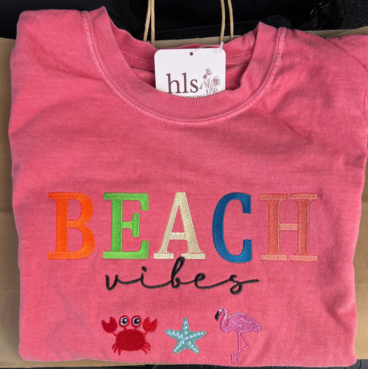 Folded pink shirt with 'BEACH vibes' text and graphics on a brown surface