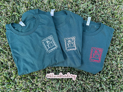 Three t-shirts with embroidered designs on a grass background
