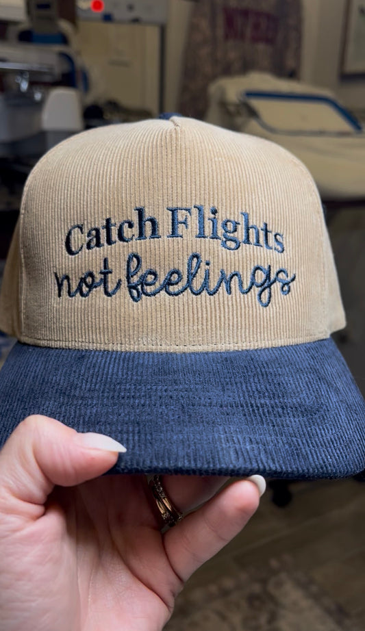 Beige and navy corduroy cap with embroidered text "catch flights not feelings"