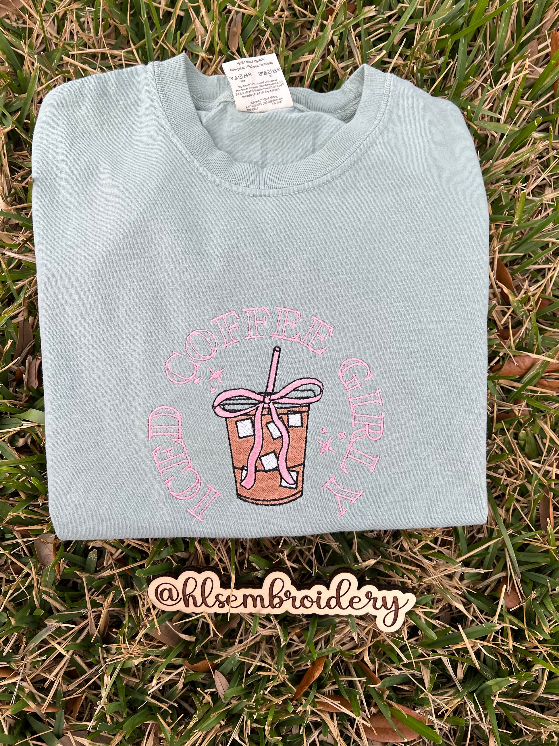 Light green t-shirt with pink graphic embroidery on grass,