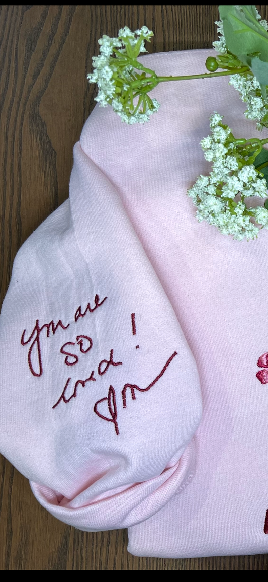 Pink crewneck with embroidered text showing a handwritten example sleeve design