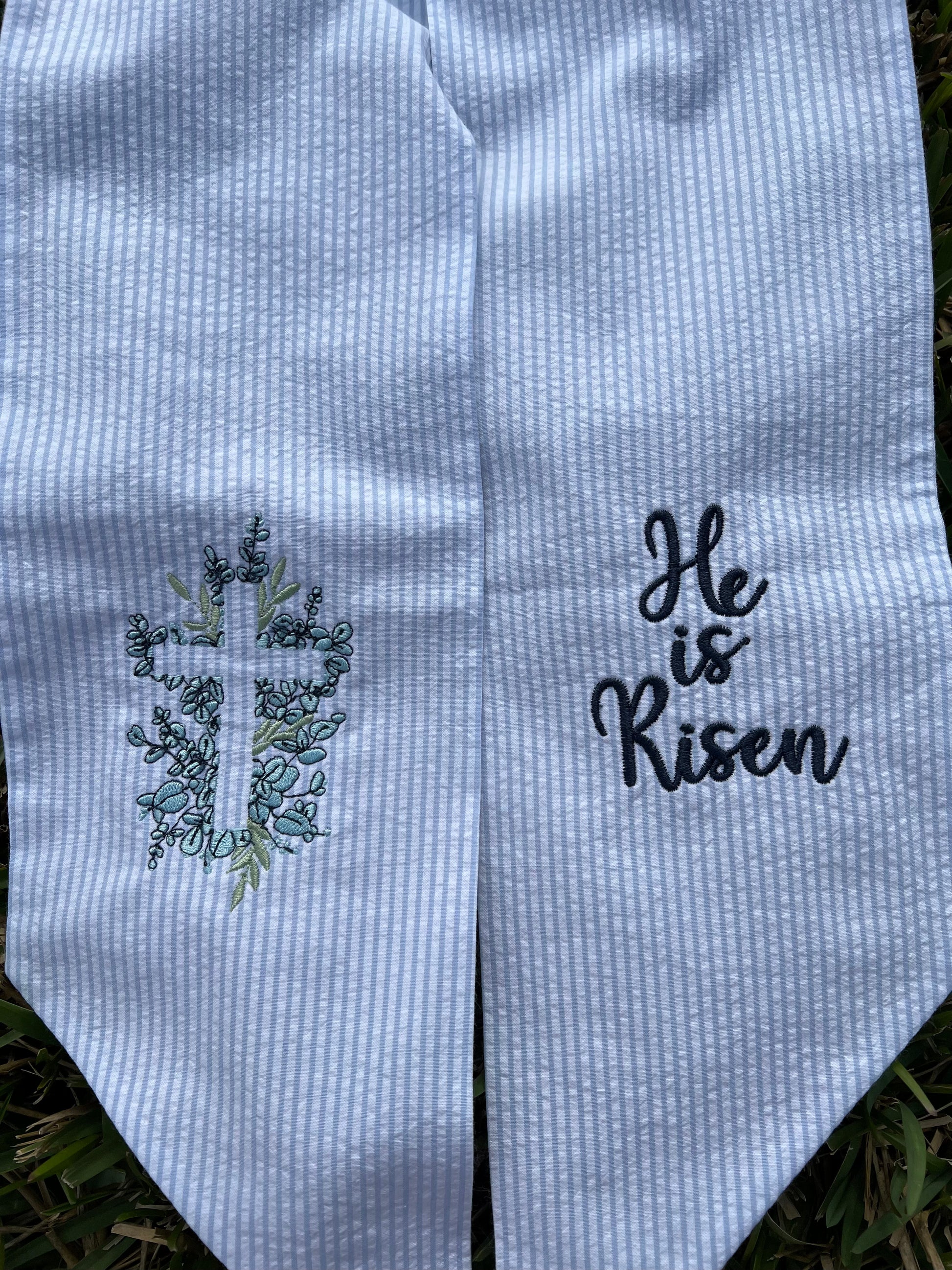 Embroidered wreath sash with cross and 'He is Risen' text on a textured fabric background