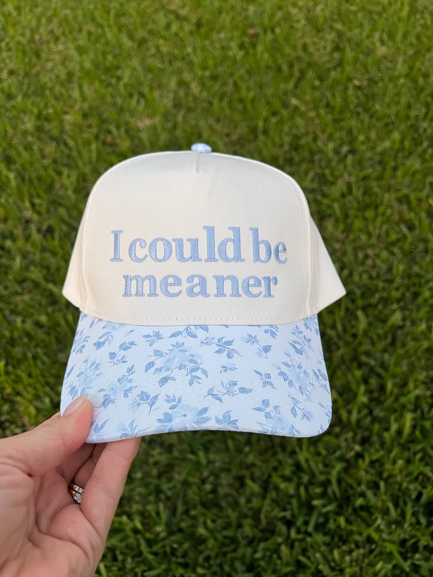Cap with 'I could be meaner' text on a grass background