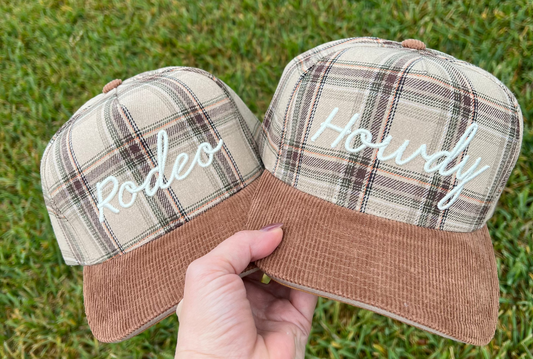 Two plaid hats with 'Rodeo' and 'Howdy' text on a grass background