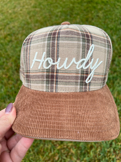 Plaid cap with 'Howdy' text held by a hand on grass
