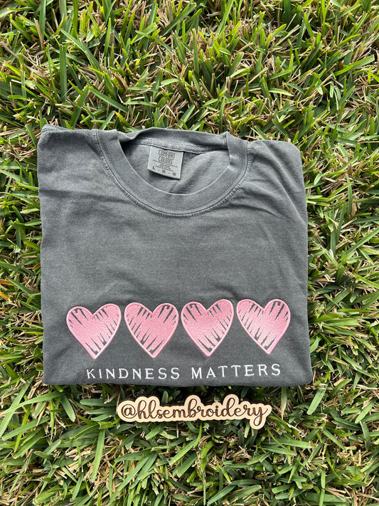 Folded color pepper comfort colors shirt with pink hearts and 'Kindness Matters' embroidered on it 