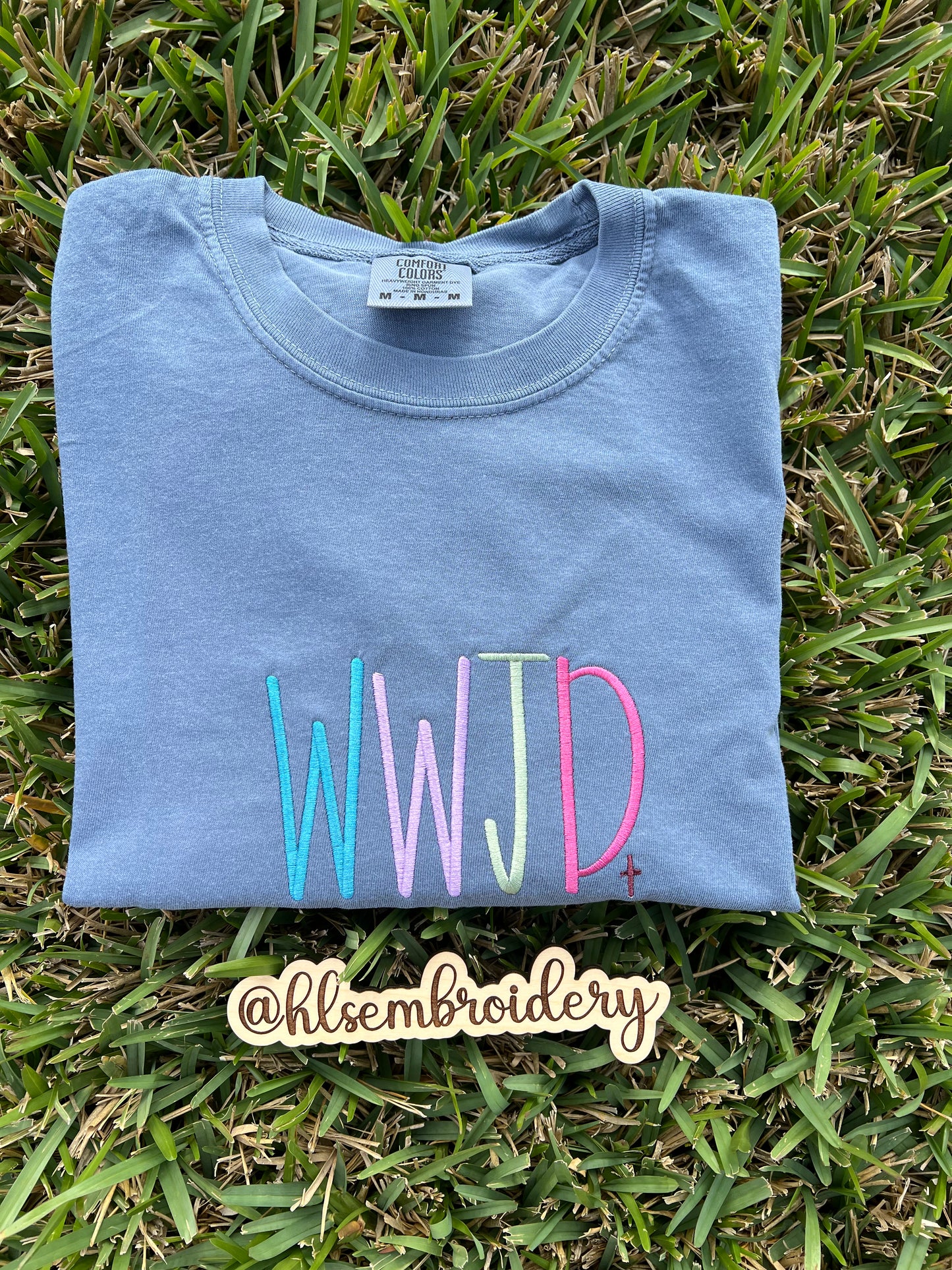 Folded blue shirt with colorful 'WWJD' text embroidered 