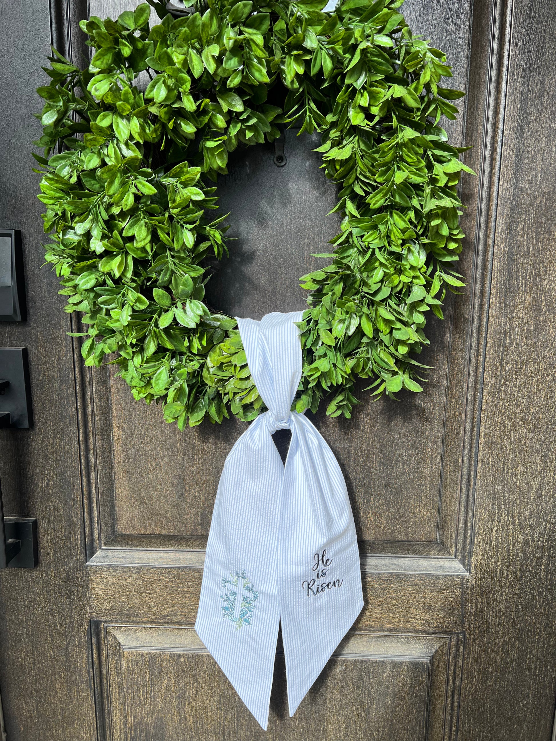 Green wreath with a blue seersucker wreath sash on a wooden door