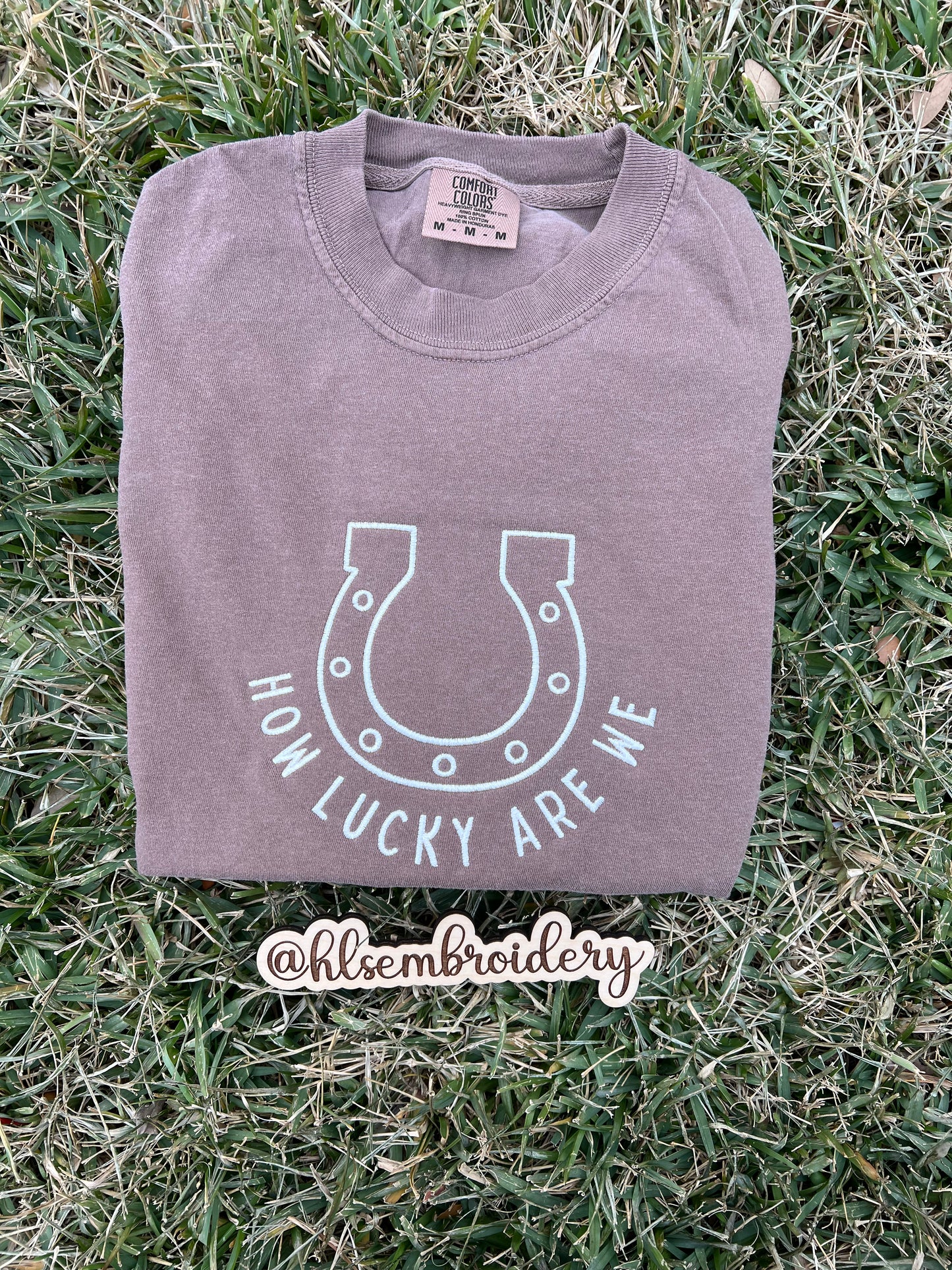 Expresso color shirt with how lucky are we and a horseshoe embroidered on the front