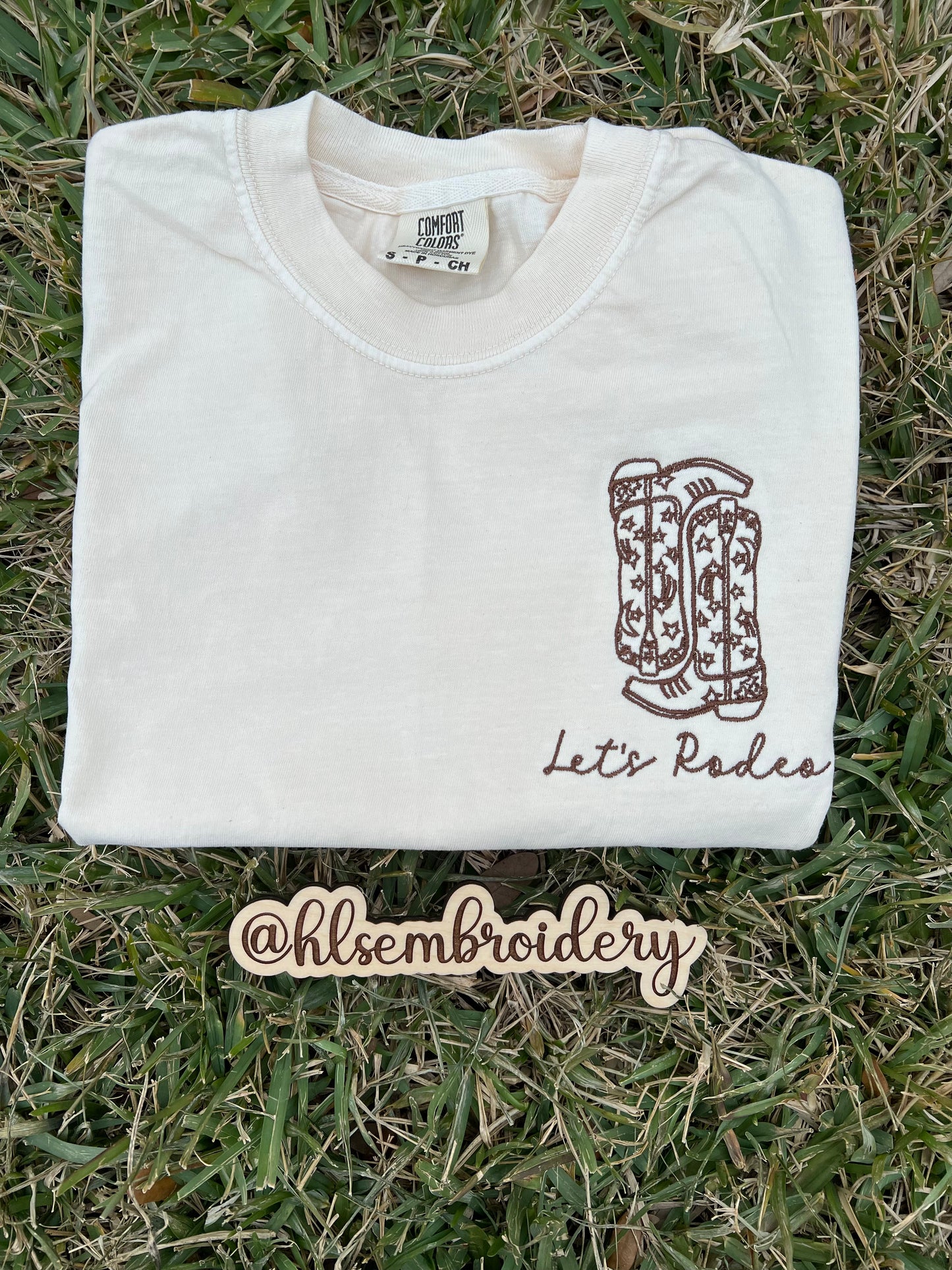 Ivory shirt with lets rodeo wording and boots embroidered on it 
