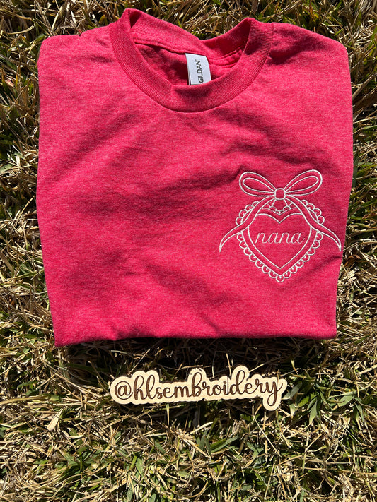 Folded red -shirt with white embroidery design on a wooden surface, featuring the brand 'hlsembroidery'.