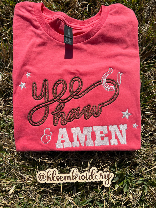 Folded pink shirt with embroidered text on grass, featuring the brand 'hlsembroidery'.