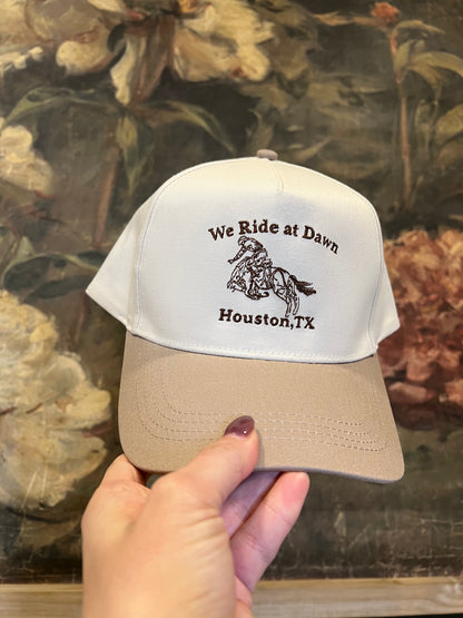 Cream and beige cap with embroidery we ride at dawn houston tx with an embroidered cowboy on a horse