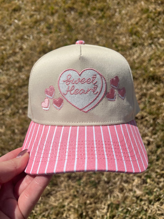Cap with 'sweet heart' design held against a grassy background