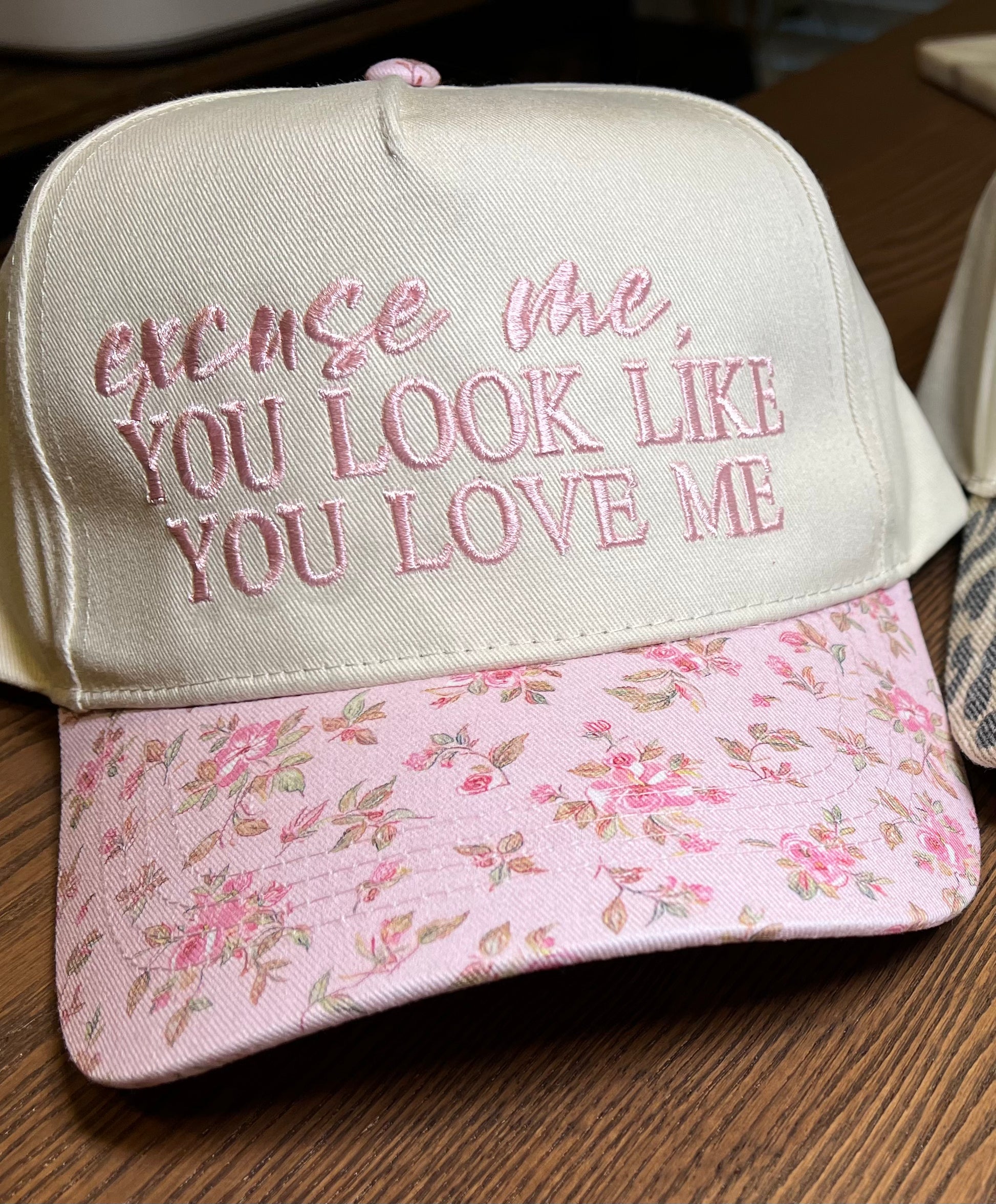 Cap with floral front and text embroidery  'excuse me, you look like you love me' on a wooden surface