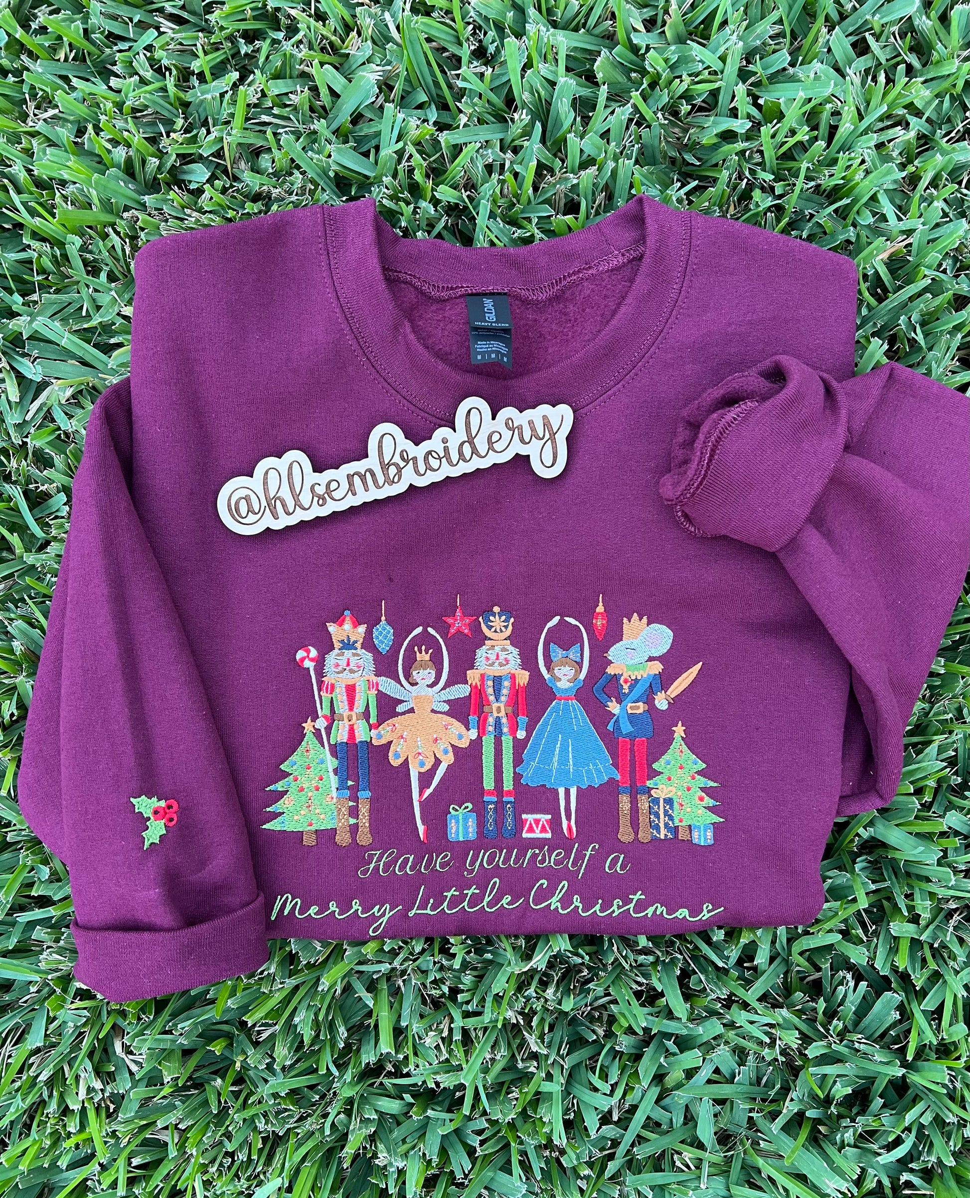maroon sweatshirt with Christmas design and 'hlsembroidery' branding on grass