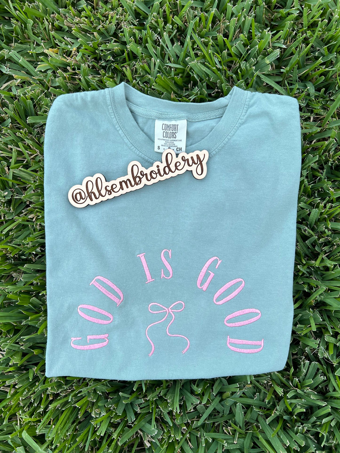 Light blue t-shirt with 'God is Good' embroidery on grass