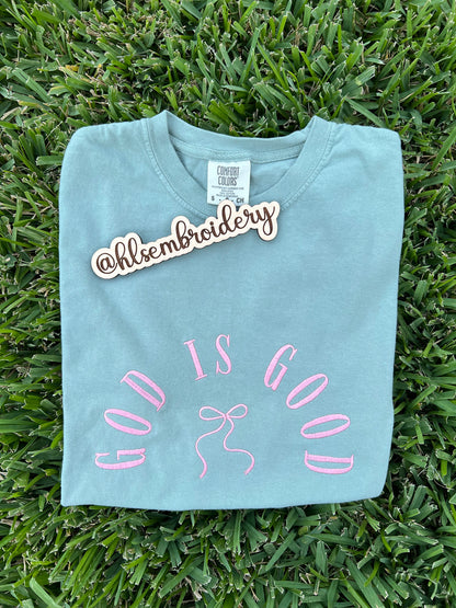 Light blue t-shirt with 'God is Good' embroidery on grass