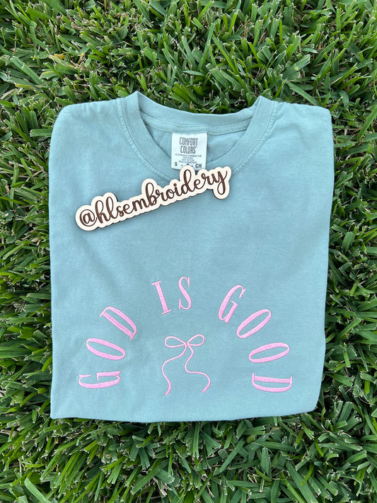 Light blue t-shirt with 'God is Good' embroidery on grass