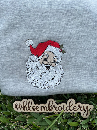 Gray sweatshirt with embroidered Santa Claus face on grass, featuring the brand 'hlsembrdery'.