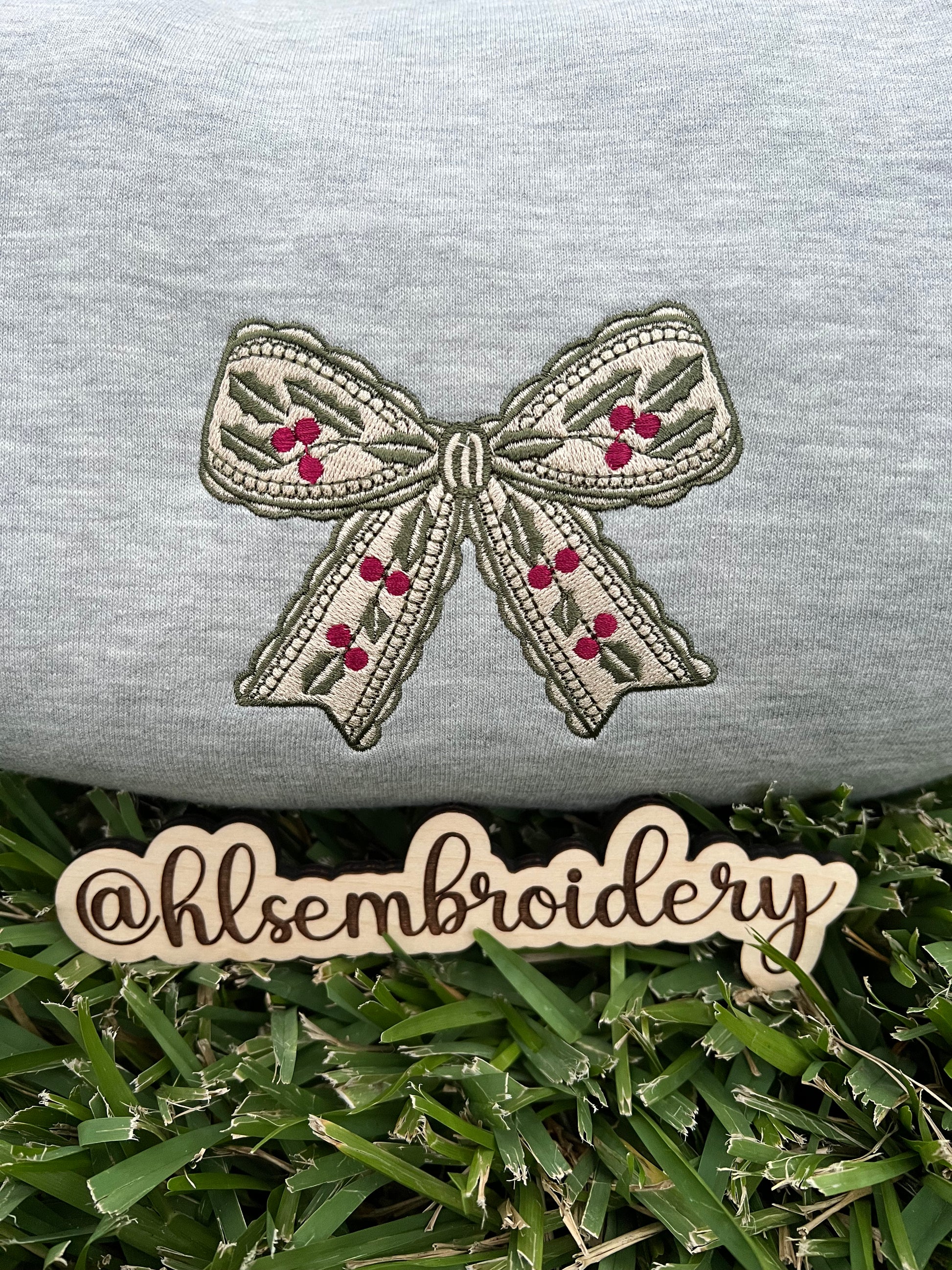 Embroidered bow design on a gray fabric with 'hlsembrodiery' branding.