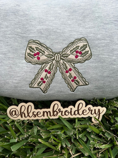Embroidered bow design on a gray fabric with 'hlsembrodiery' branding.