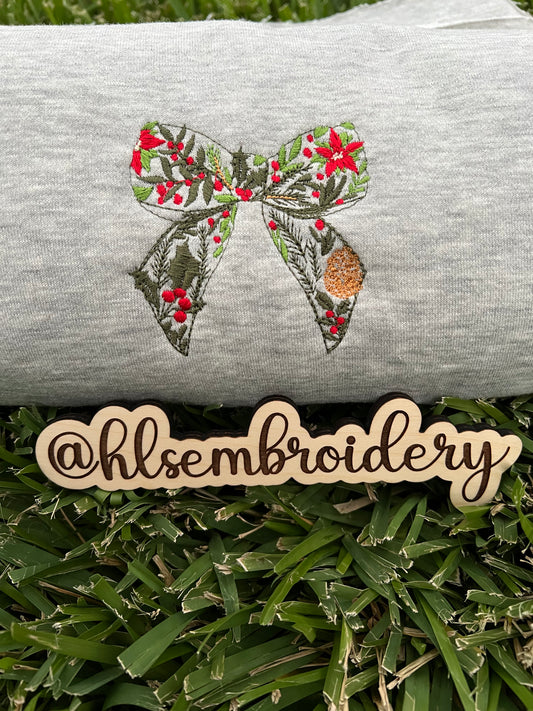 Embroidered bow design on a gray fabric with 'hlsembrodiery' branding.