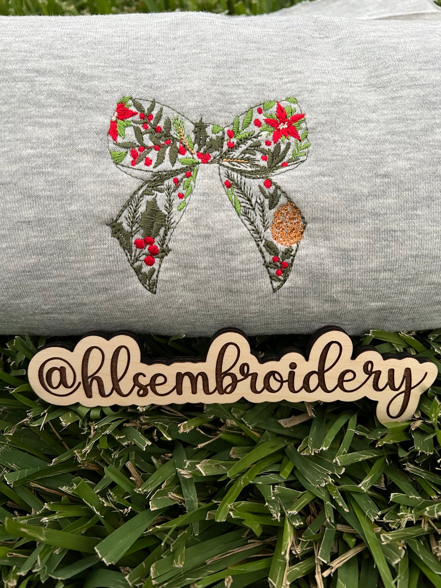 Embroidered bow design on a gray fabric with 'hlsembrodiery' branding.